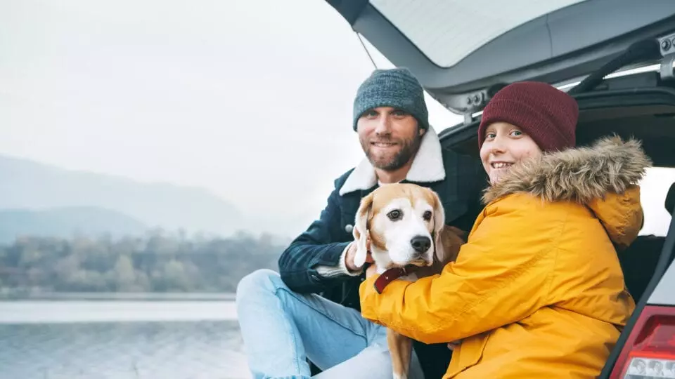 Father and son sitting in the trunk of an SUV with their dog