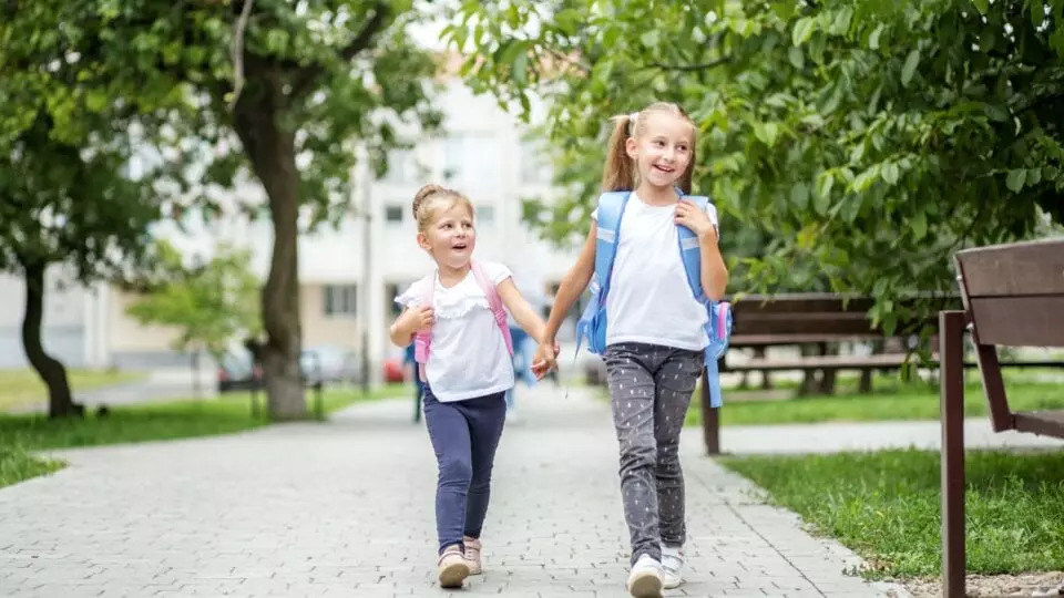 Two girls holding hands with backpacks on