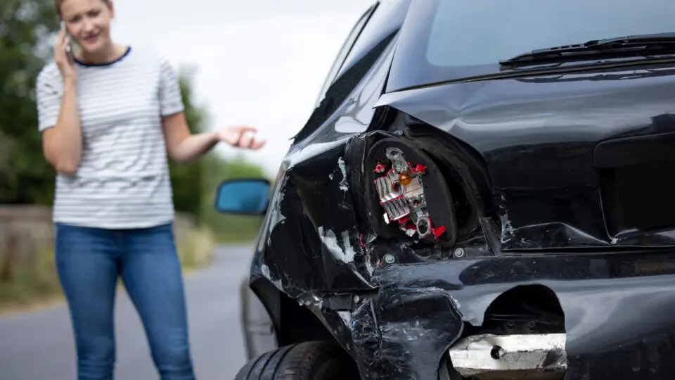 Female standing beside her car after a collision.