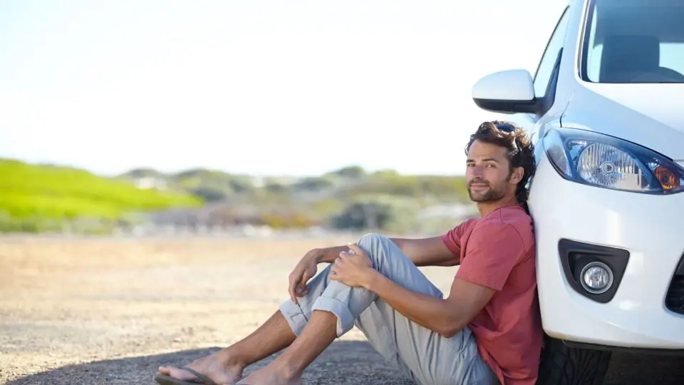 Man sitting on the road, leaning against his car