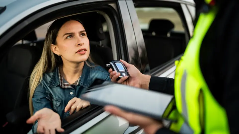 A woman in her car being asked to take a breathalyzer test