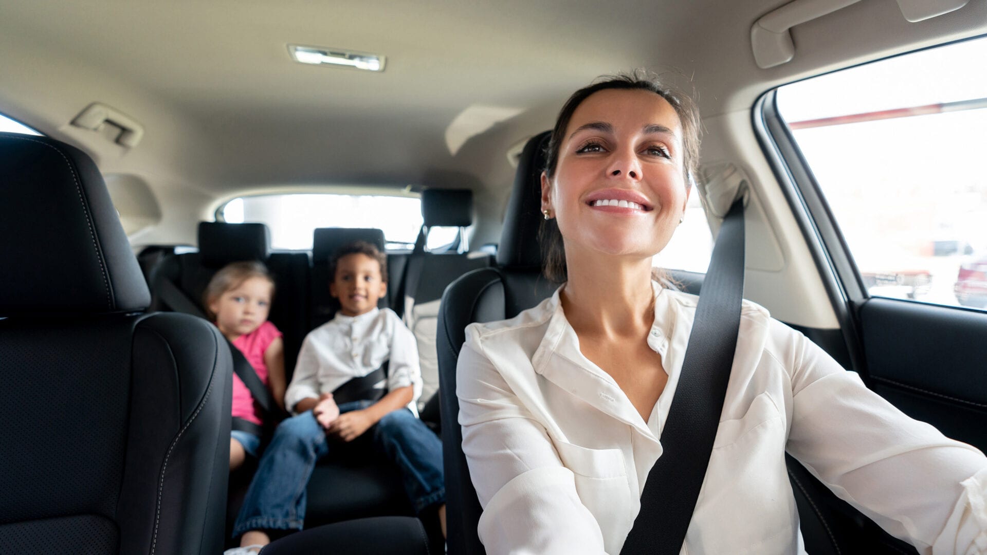 Woman smiling while driving, checking on two kids in rearview mirror