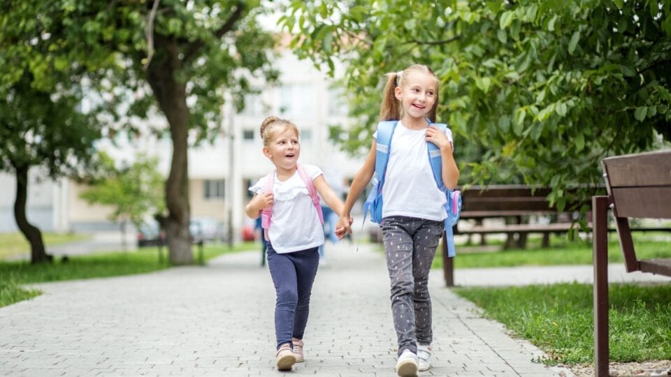 Two girls holding hands with backpacks on