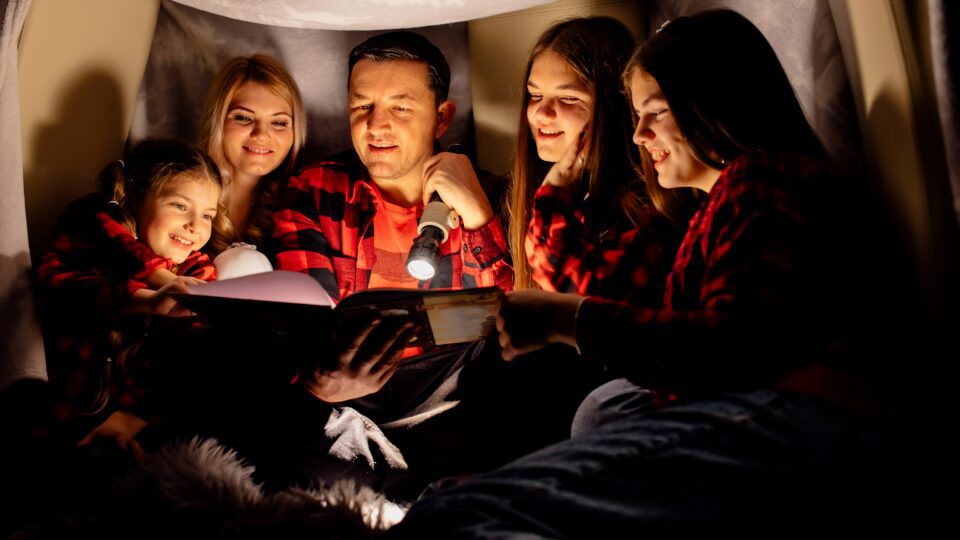 family reads book with a flashlighty during a power outage
