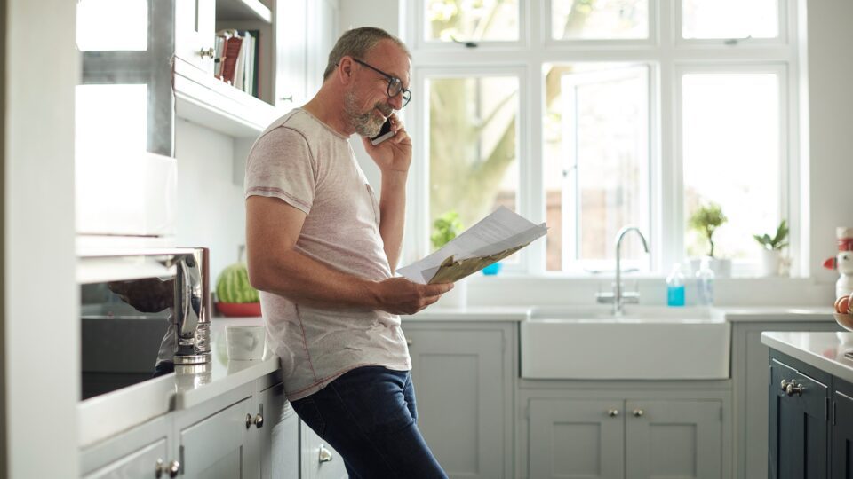 Man in his kitchen reading mail on his phone